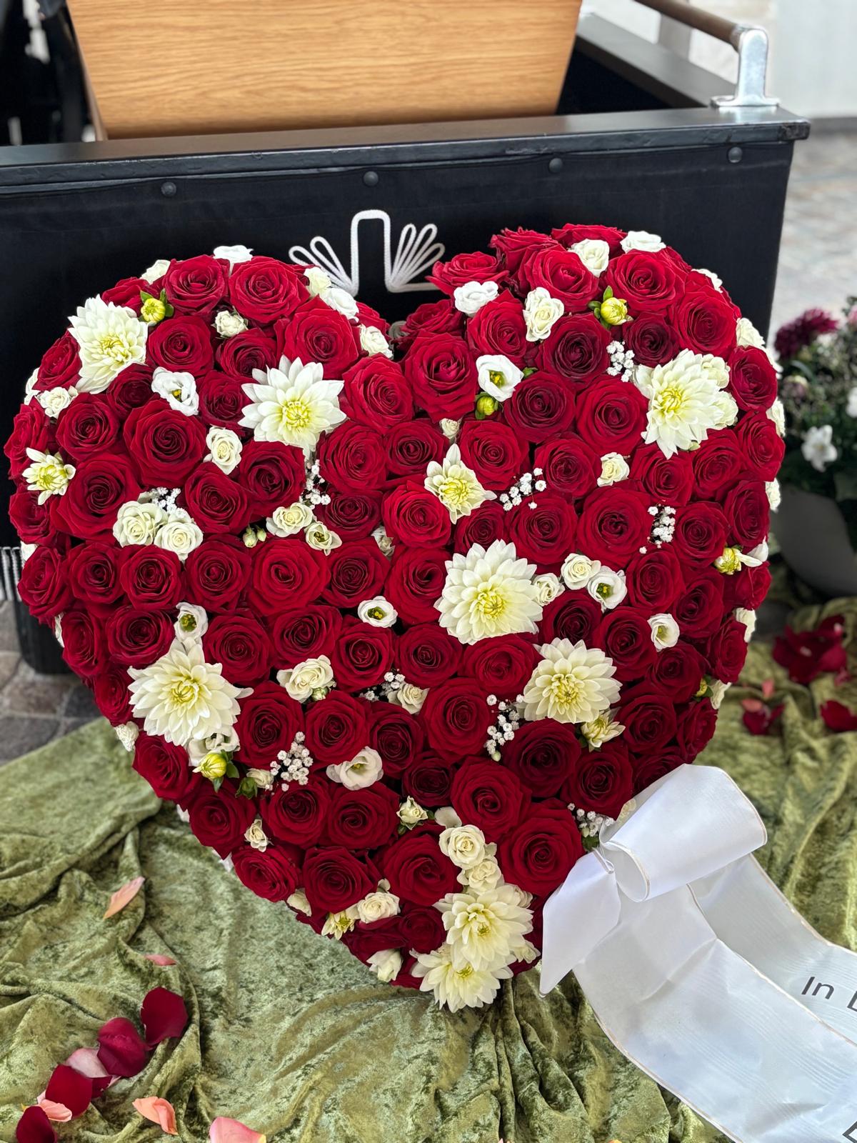 Herzförmiger Trauerschmuck aus roten Rosen und weißen Blüten