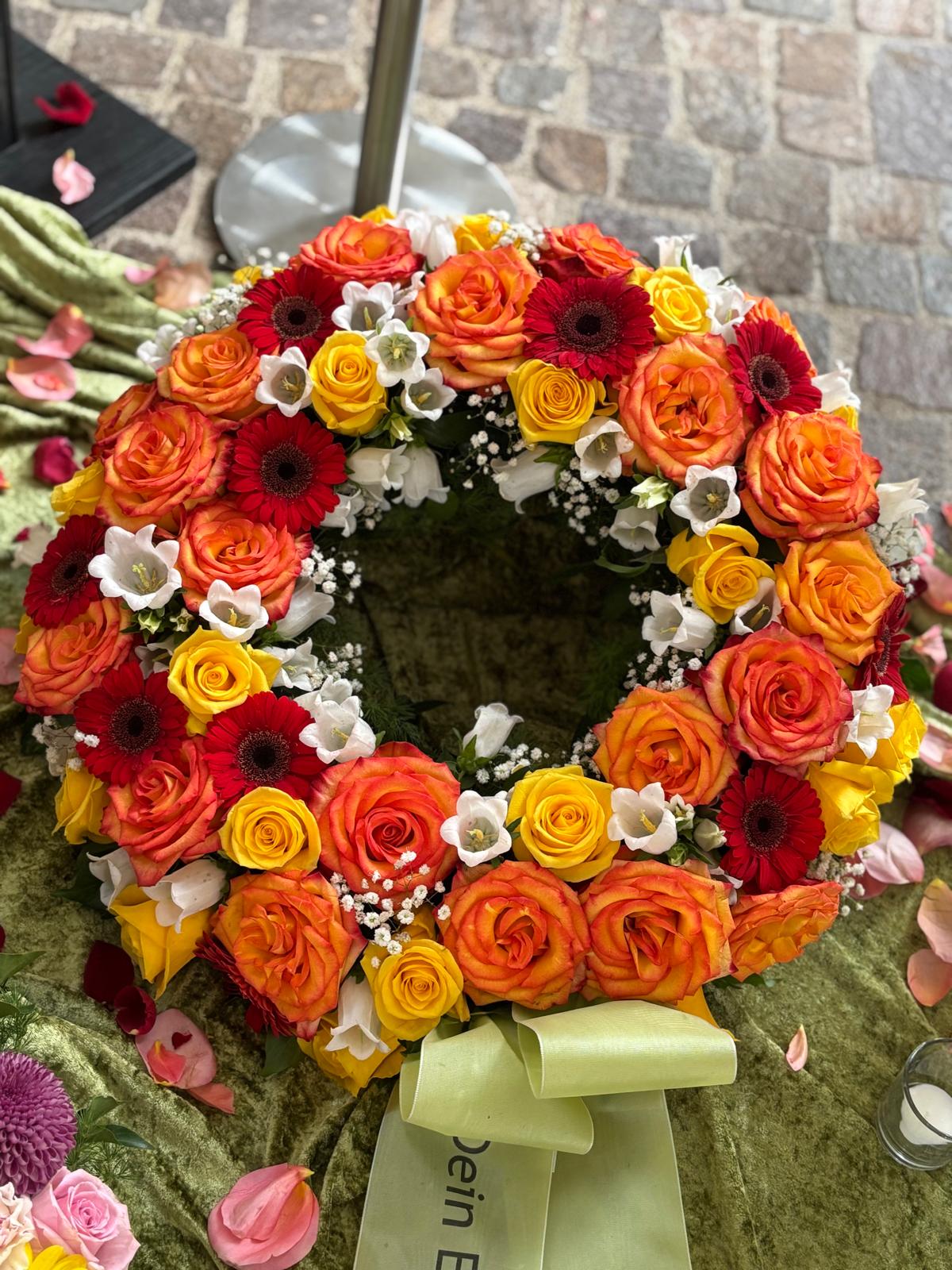 Trauerkranz mit Rosen in Orange und Gelb, weißen Blüten und Schleife