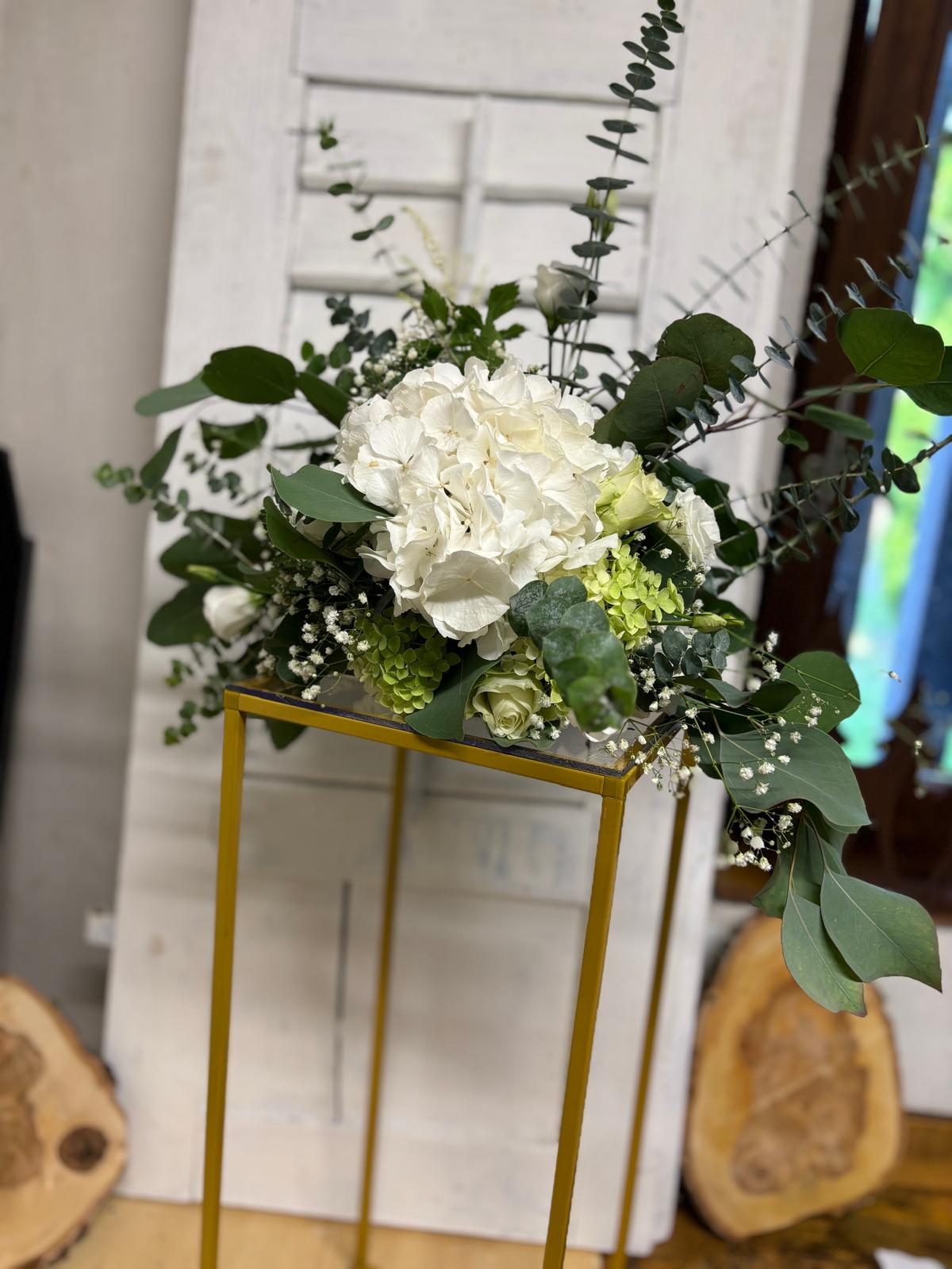 Tischdekoration mit weißen Hortensien, Rosen und Eukalyptus auf einem goldfarbenen Gestell