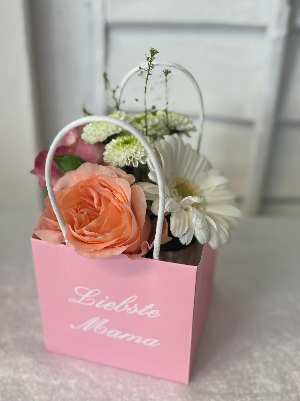 Blumen in einer rosa Geschenktasche mit dem Schriftzug Beste Mama